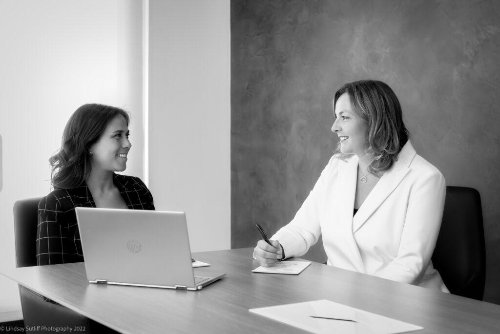 two women in professional attire sitting at  table and talking