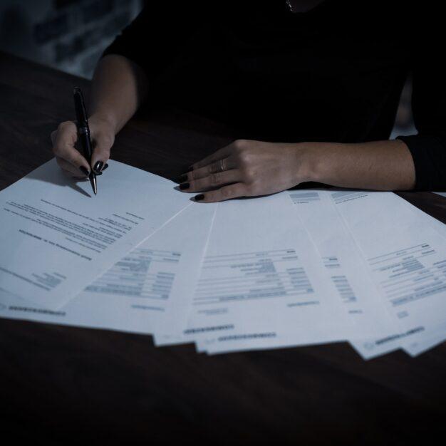 a woman signing a document with several papers laid out in a fan shape
