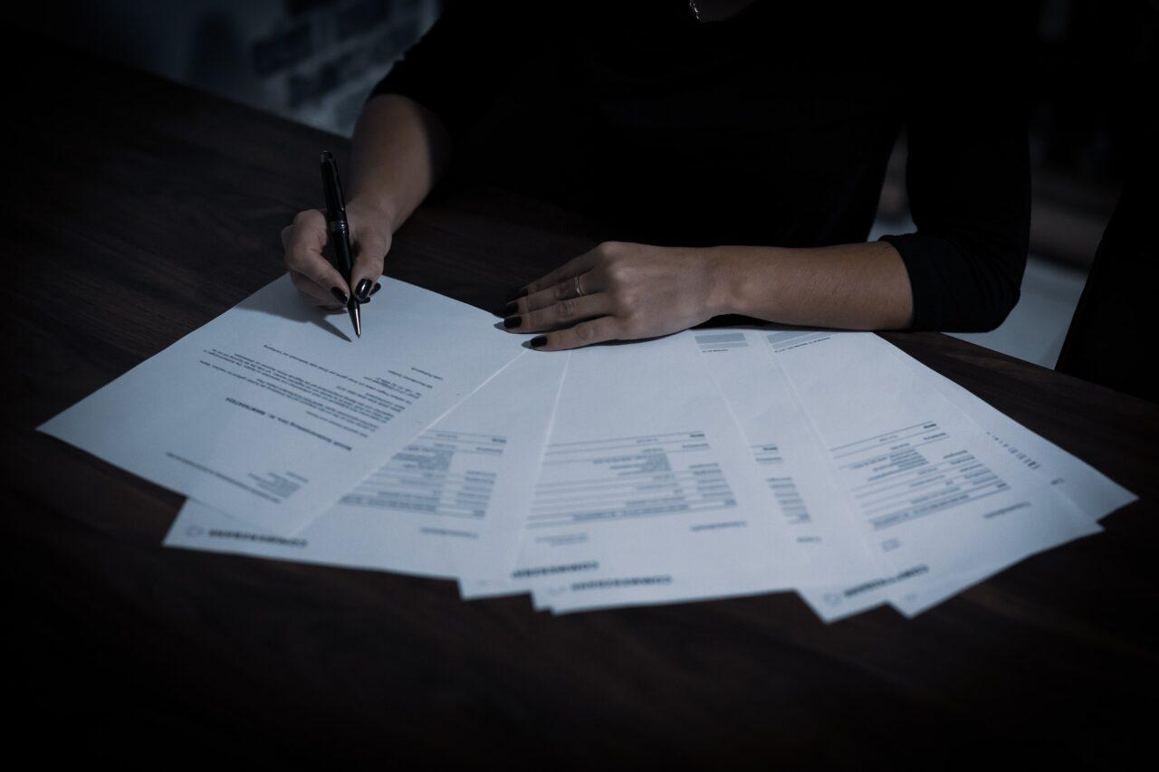a woman signing a document with several papers laid out in a fan shape