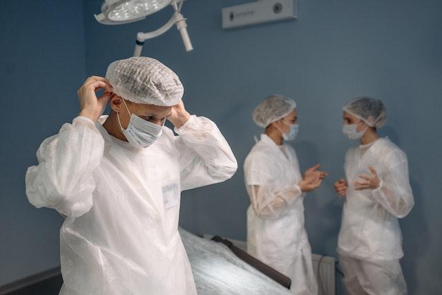 a surgeon putting on a hair net with two other surgeons in the background