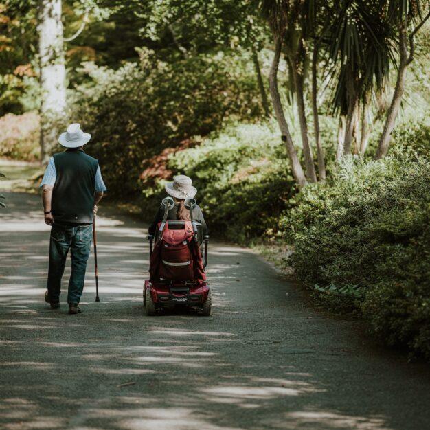 two people on a paved path, one is walking and the other is in a mobility chair