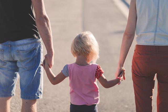 a child walking between and holding hands with two adults at their sides