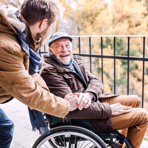 a person leaning over an elderly man in a wheelchair who is smiling