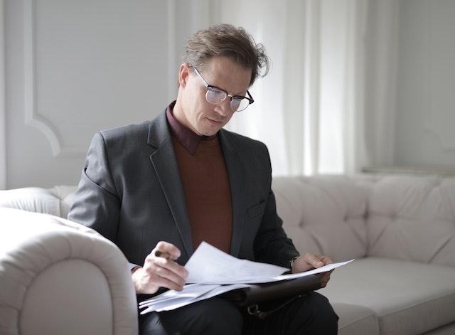 man sitting on a couch and looking through paperwork in his lap