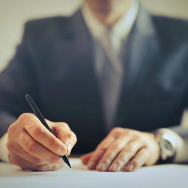 a man in a suit sitting at a desk and writing something down
