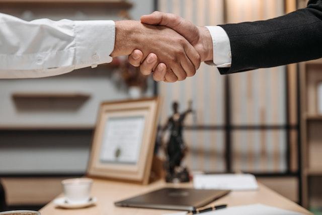 two people in formal clothing shaking hands over a desk