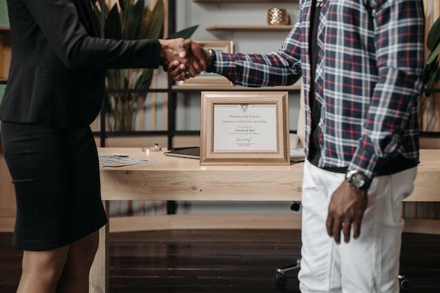 a woman in formal clothes shaking hands with a man in casual clothes