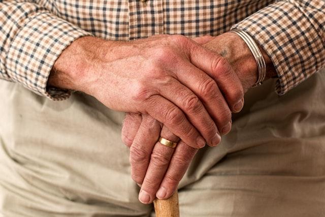 an elderly person's hands folded on the top of a cane