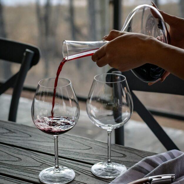 a person pouring wine from decanter into a wine glass on a table