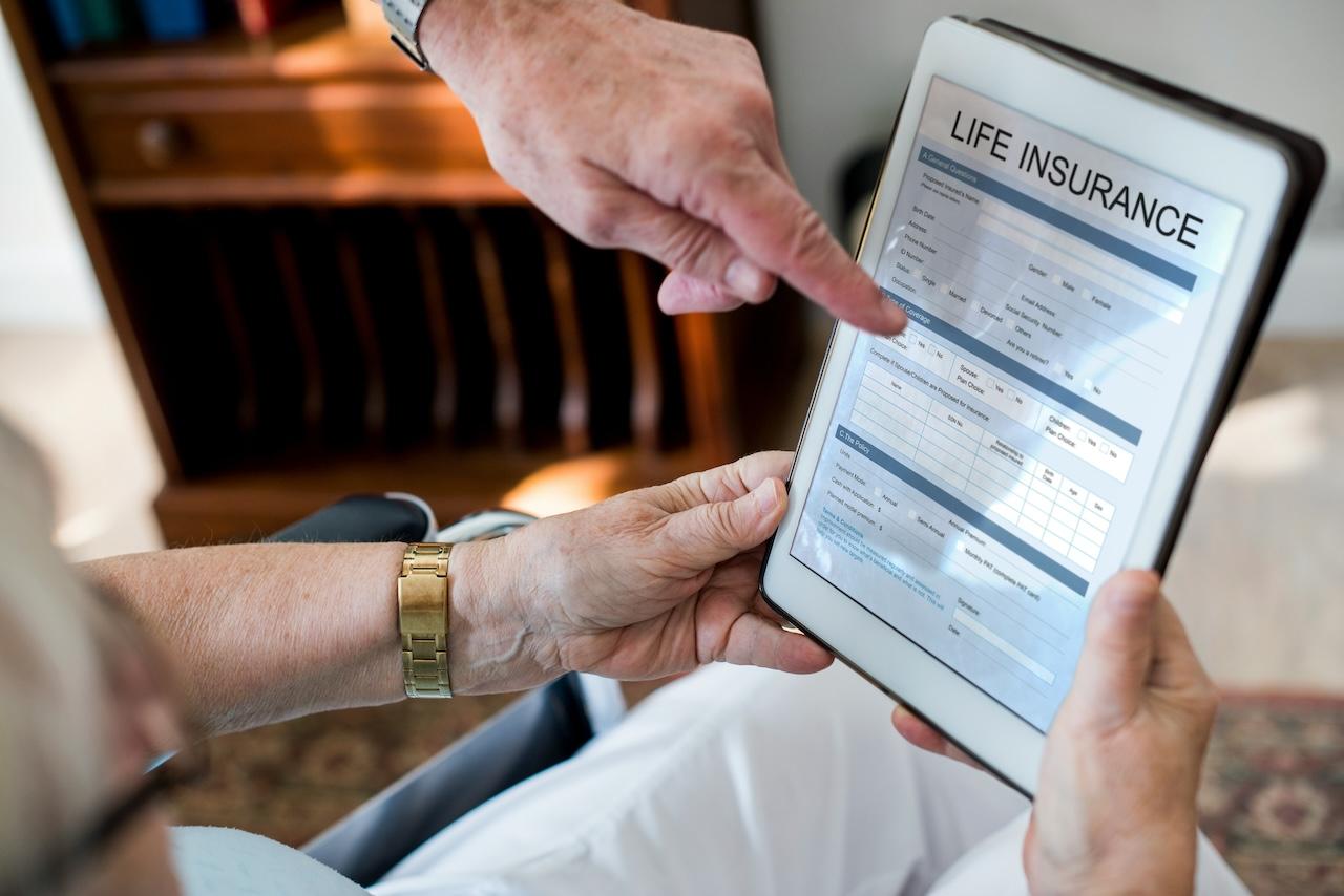 an elderly person holding a tablet computer which displays a document titled "life insurnace"