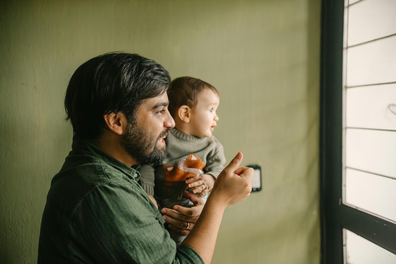 a young man holding a boy in his arms, both looking out a window